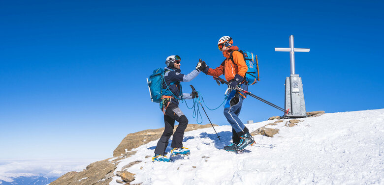 Zwei Skitourengeher erreichen den Gipfel des Berges Großer Geiger bei Kaiserwetter.