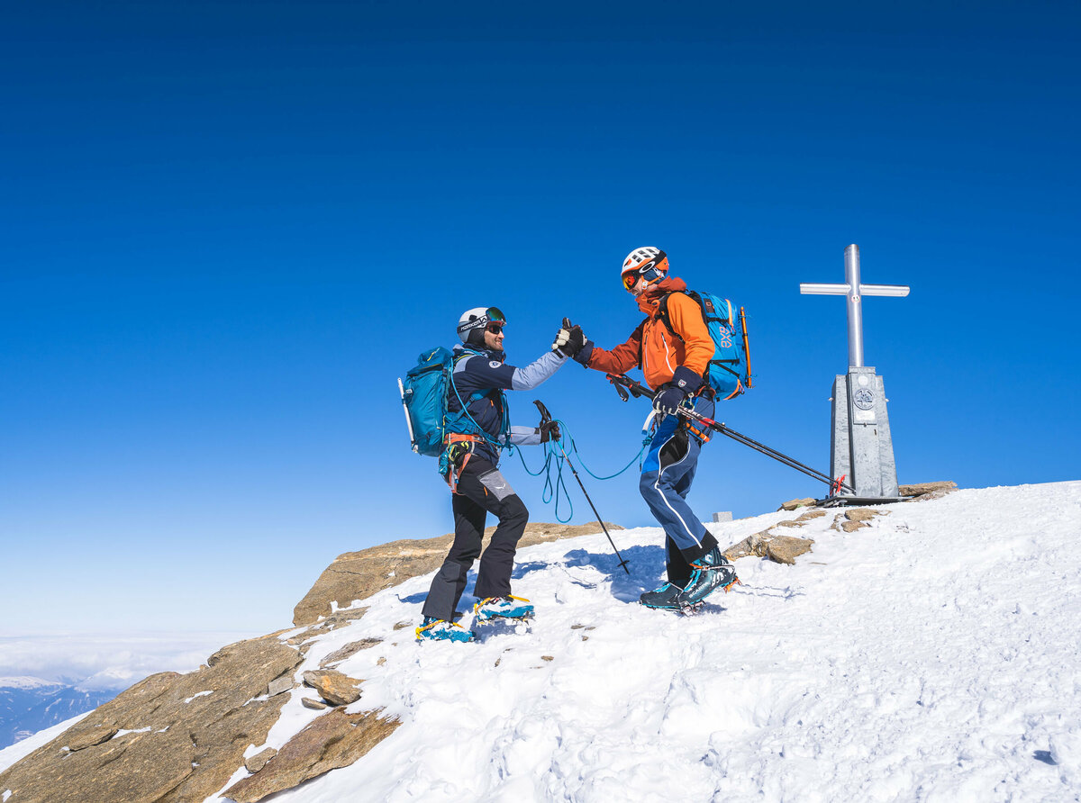 Zwei Skitourengeher erreichen den Gipfel des Berges Großer Geiger bei Kaiserwetter.