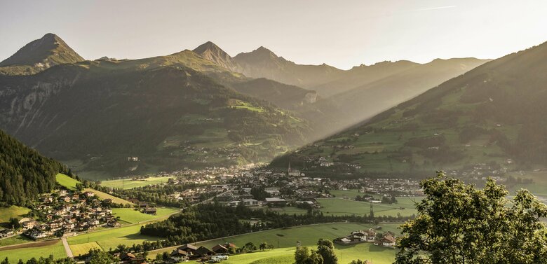 Blick von oben auf Matrei in Osttirol an einem Sommertag. Die Sonnenstrahlen blitzen auf das Dorf.
