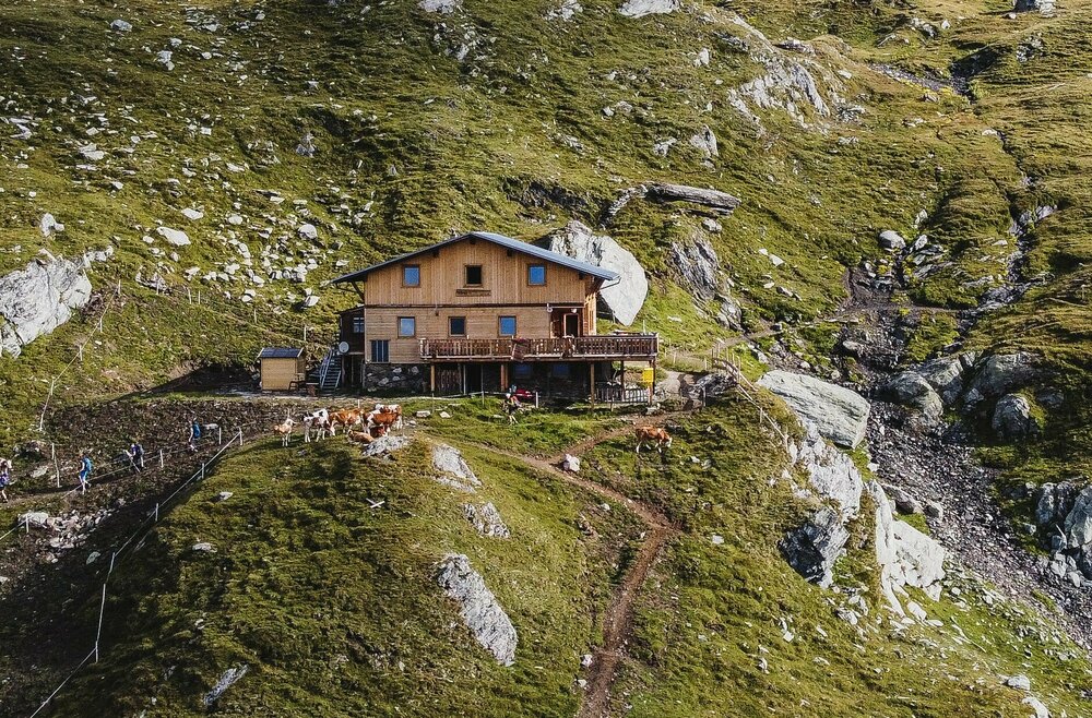Die neue Eisseehütte hebt sich sanft von der Landschaft hervor, die von grauen Felsen und grünen Almwiesen gesäumt ist.