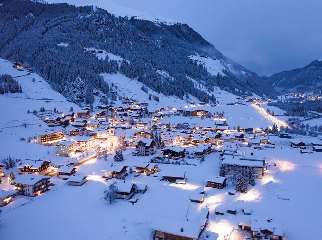 Blick auf das winterliche, beleuchtete St. Jakob im Defereggental am Abend.
