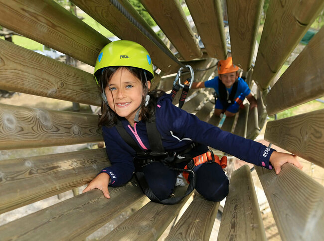 Aufnahme in ein hölzernes Rohr im Hochseilgarten in Sillian, wo zwei Kinder am Klettern sind.