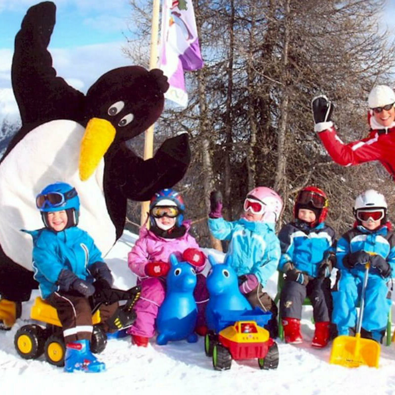 Kinder mit ihrem Skilehrer und einem Pinguin-Maskottchen im Skizentrum Hochpustertal