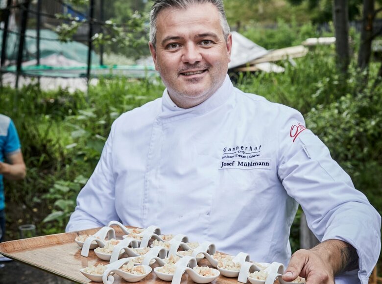 Josef Mühlmann vom Gannerhof präsentiert auf einem Tableau in seinen Hände die von ihm zubereiteten und angerichteten Gerichte auf weißen Löffeln.