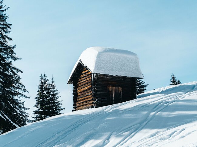 Frisch verschneite kleine Holzhütte bei blauen Himmel in Obertilliach