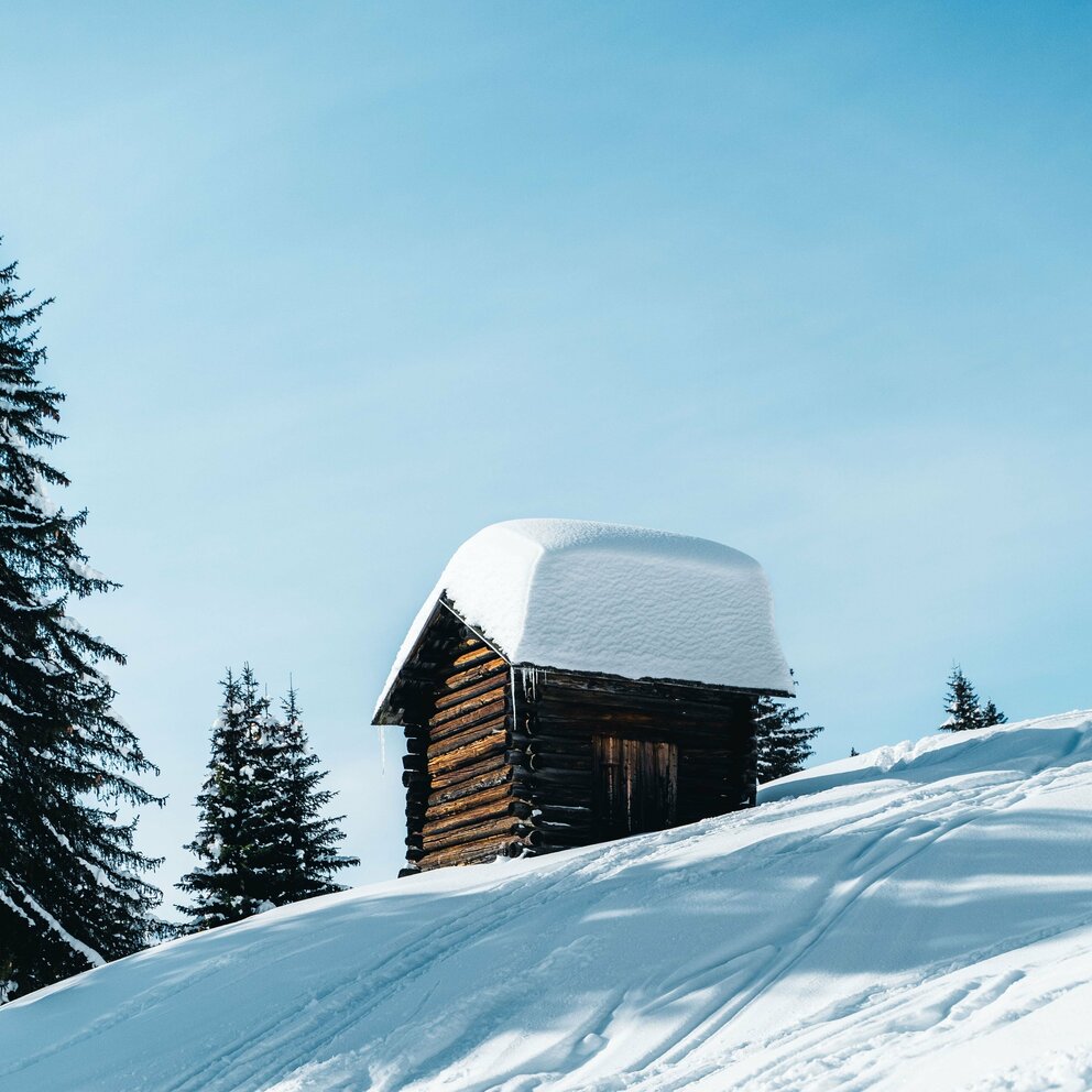 Frisch verschneite kleine Holzhütte bei blauen Himmel in Obertilliach