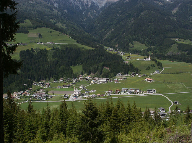 Luftaufnahme der Ortschaft Strassen im Sommer mit grünen Feldern und Wäldern.
