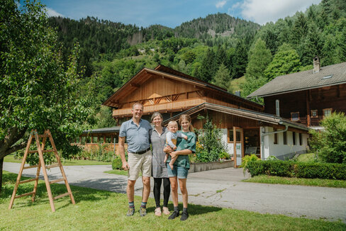 Eine Familie steht in der grünen Wiese vor einem schön renovierten Bauernhaus