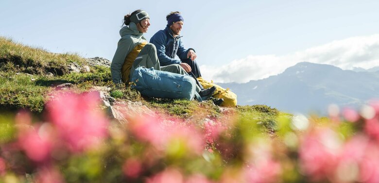 Ein Paar macht eine Pause auf einer Wiese mit Almrosen auf dem Weg zum Bösen Weibele zu einer Sonnenaufgangstour.