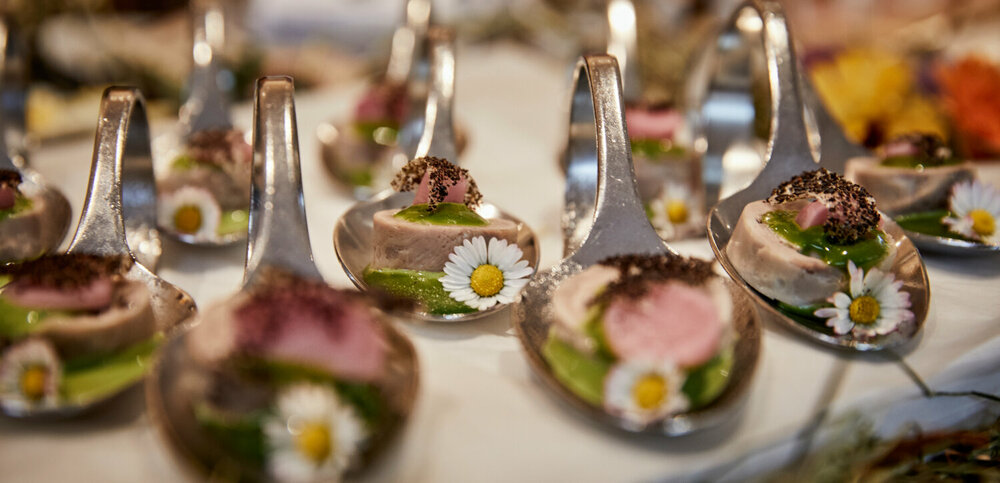Haubenküche im Gannerhof - Gericht bestehend aus einem runden Fleischstück mit einer grünen Soße verziert mit einem Gänseblümchen auf einem Löffel angerichtet.