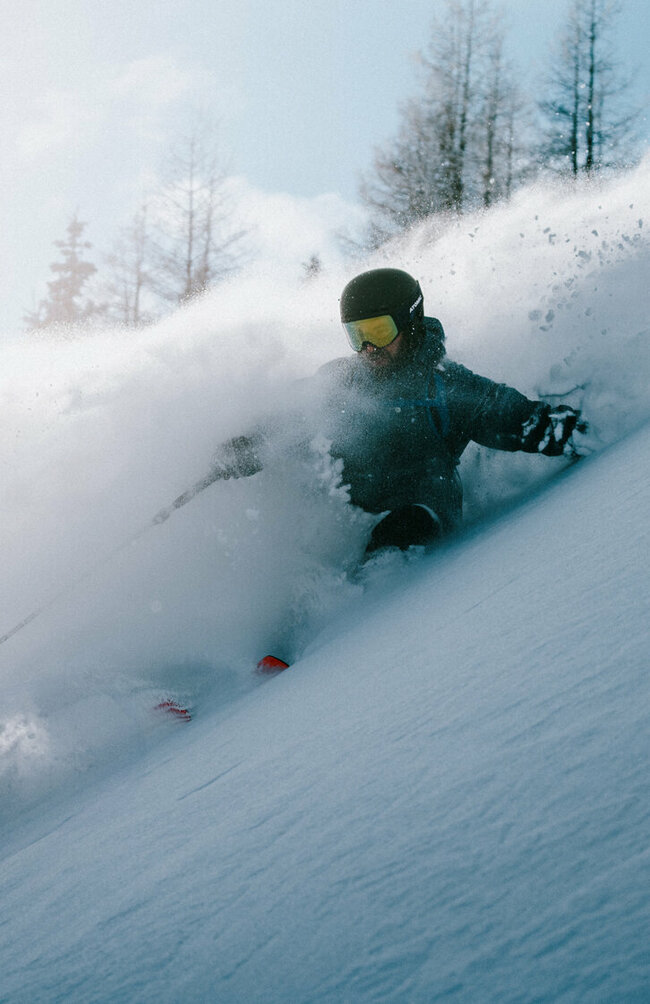 Ein Skitourenfahrer bei der Abfahrt von der Roten Wand im Defereggental. Er fährt durch Tiefschnee und Trägt Helm, Skibrille und Stöcke. 