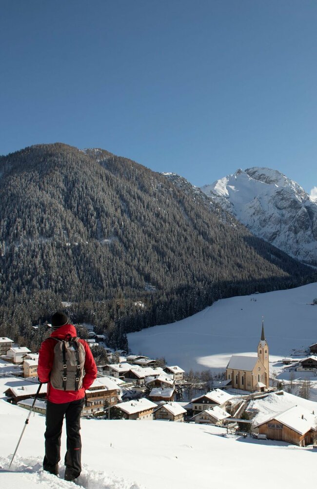 Zwei Personen genießen beim Winterwandern den Ausblick auf das Dorf Kartitsch.