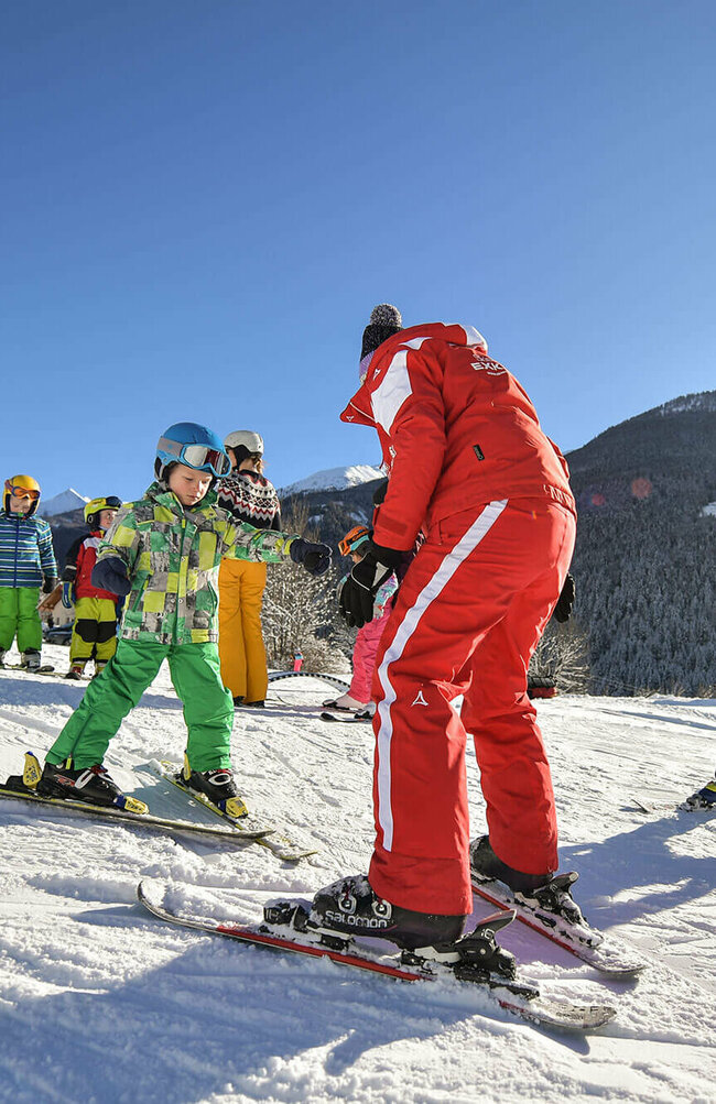 Ein rot gekleideter Skilehrer mit mehreren Kindern bei Traumwetter am Fellach Lift in Virgen.