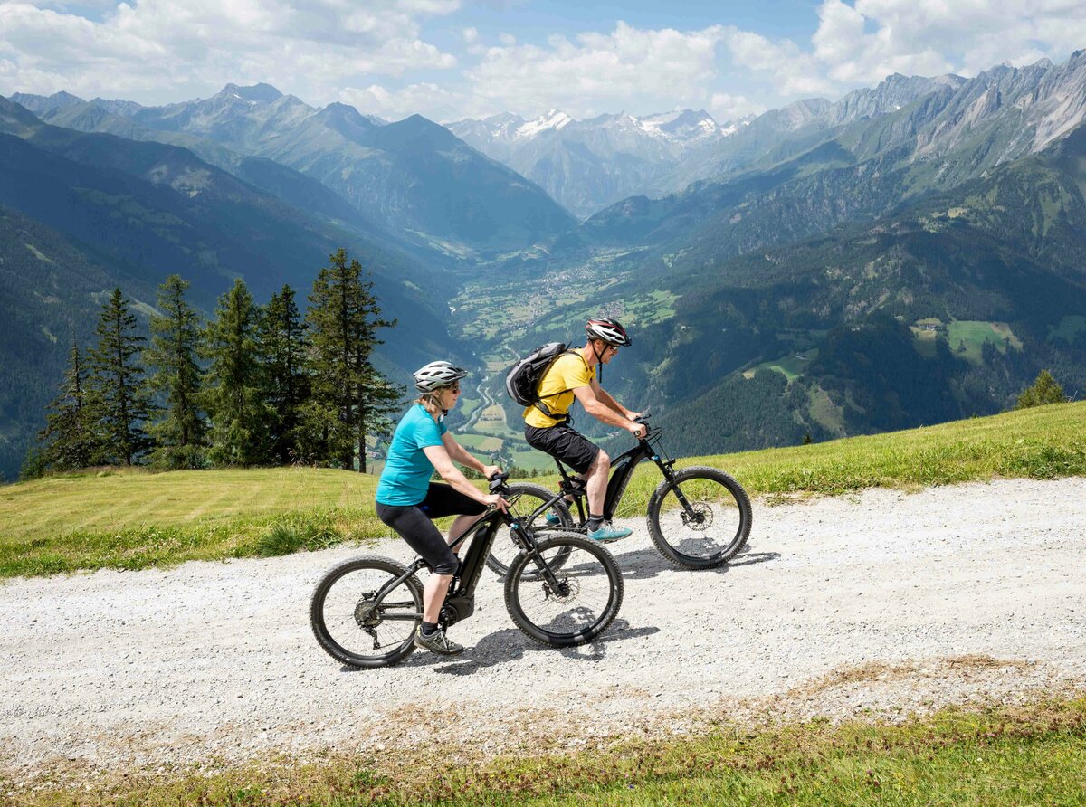 Mountainbiken am Klaunzerberg Zwei Personen auf E-Mountainbikes auf einem breiten Weg am Klaunzerberg. Im Hintergrund erstreckt sich das Tal und die umliegende Berglandschaft.