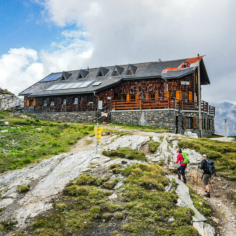 Zwei Personen mit Wanderstöcken auf den letzten Metern vor der Badener Huette am Adlerweg in Osttirol.