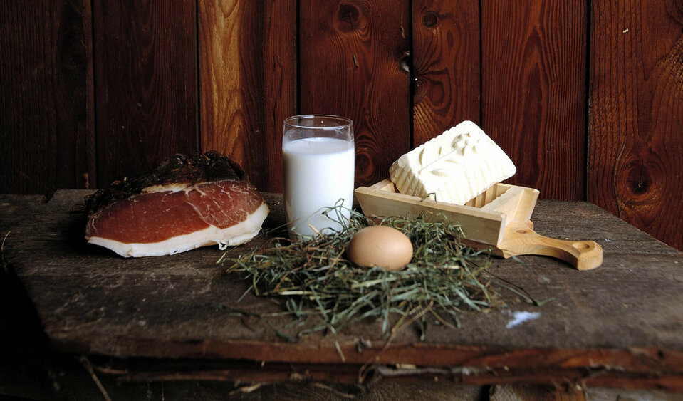 Speck, Butter, Milch und Ei aus eigener Hofproduktion auf einem Brett anschaulich positioniert.