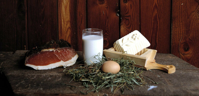 Speck, Butter, Milch und Ei aus eigener Hofproduktion auf einem Brett anschaulich positioniert.