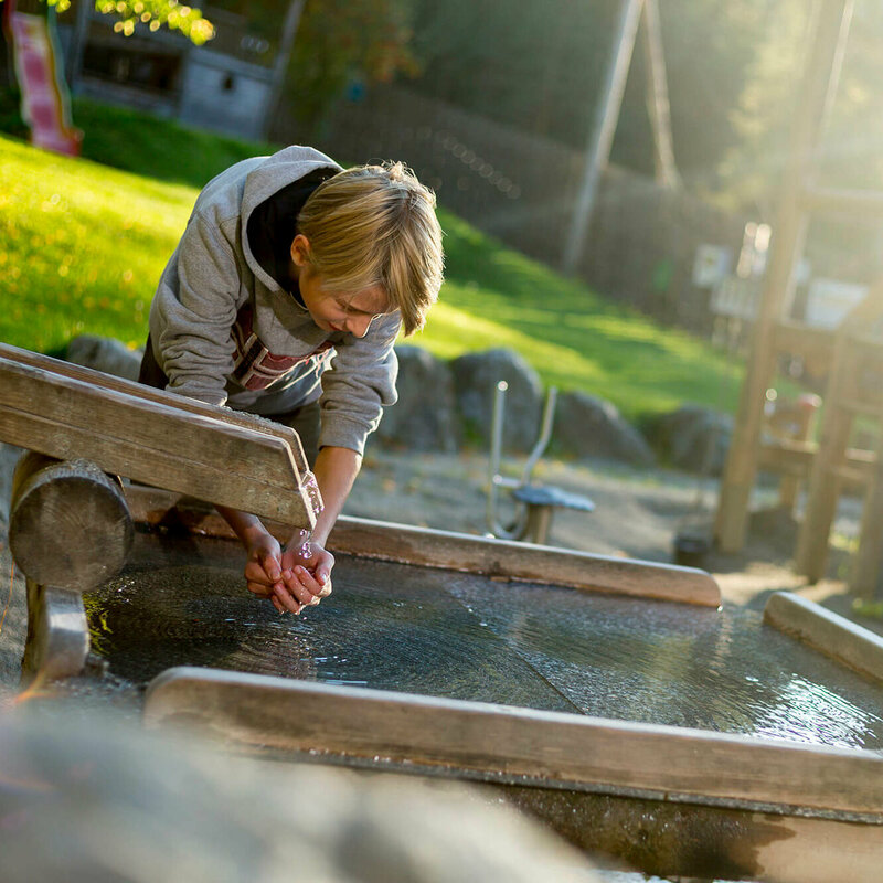 Ein Junge hält seine Hände ins Wasser bei einer Wasserstelle am Spielplatz in der Galitzenklamm.