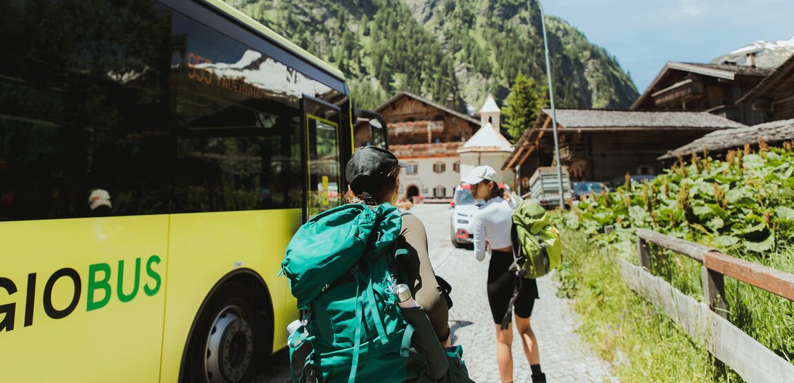 Zwei Wanderer steigen aus dem gelben Linienbus der ÖBB aus, im Hintergrund steht der traditionsreiche Gasthof „Matreier Tauernhaus“ in Matrei in Osttirol.