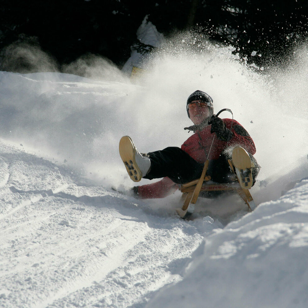 Rodel Leckfeldalm Rodelbahn Da staubt der Pulverschnee, als der Rodler die Kurve einer Rodelbahn nimmt. Ein natürlcher Schneewall begrenzt die Bahn.