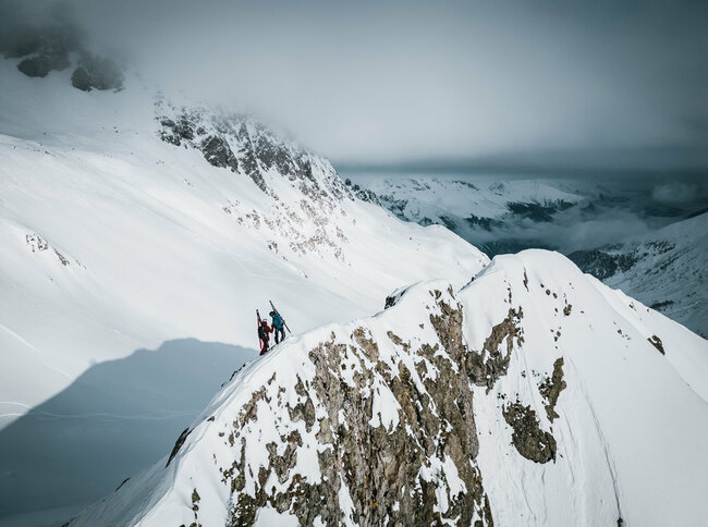 Zwei Skitourengeher stehen am Gipfel der Roten Wand im Osttiroler Defereggental. Außerdem sieht man die frisch verschneite Landschaft im Hintergrund.