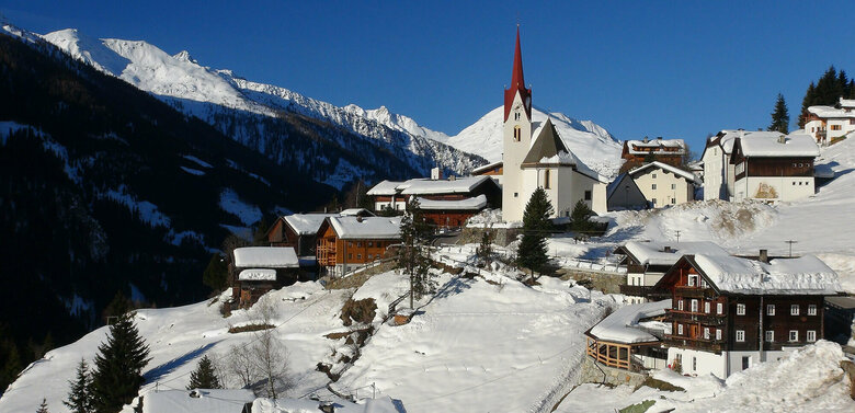 Blick auf das winterliche St. Veit im Defereggen, mit Blick auf die Kirche im Zentrum und einem blauen Himmel darüber.