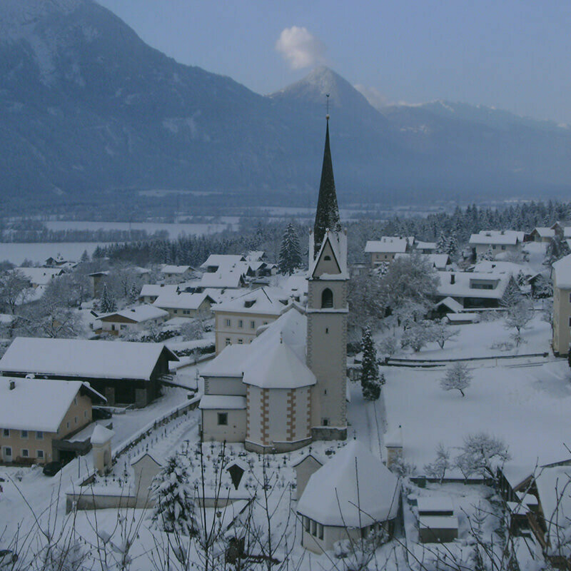 Die Kirche in Nikolsdorf liegt im Schnee an einem trüben Wintertag.