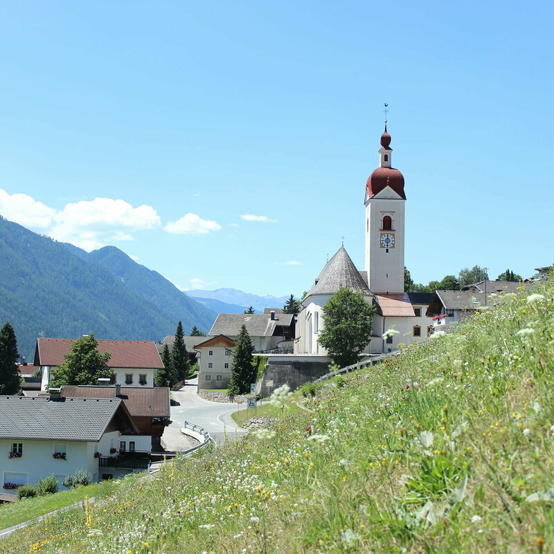 Ortsansicht von Assling mit einer sommerlichen Wiese im Vordergrund