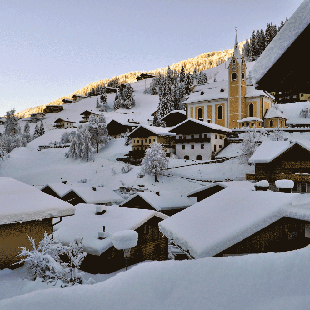 Ausservillgraten mit schneebedeckten Dächern und der Kirche im Winter.