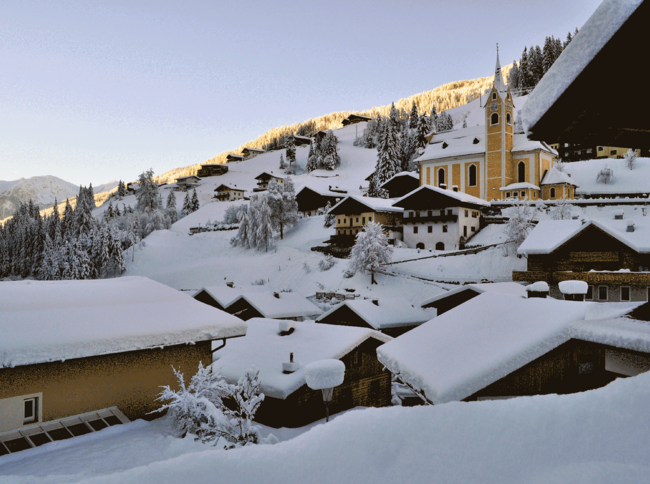 Ausservillgraten mit schneebedeckten Dächern und der Kirche im Winter.