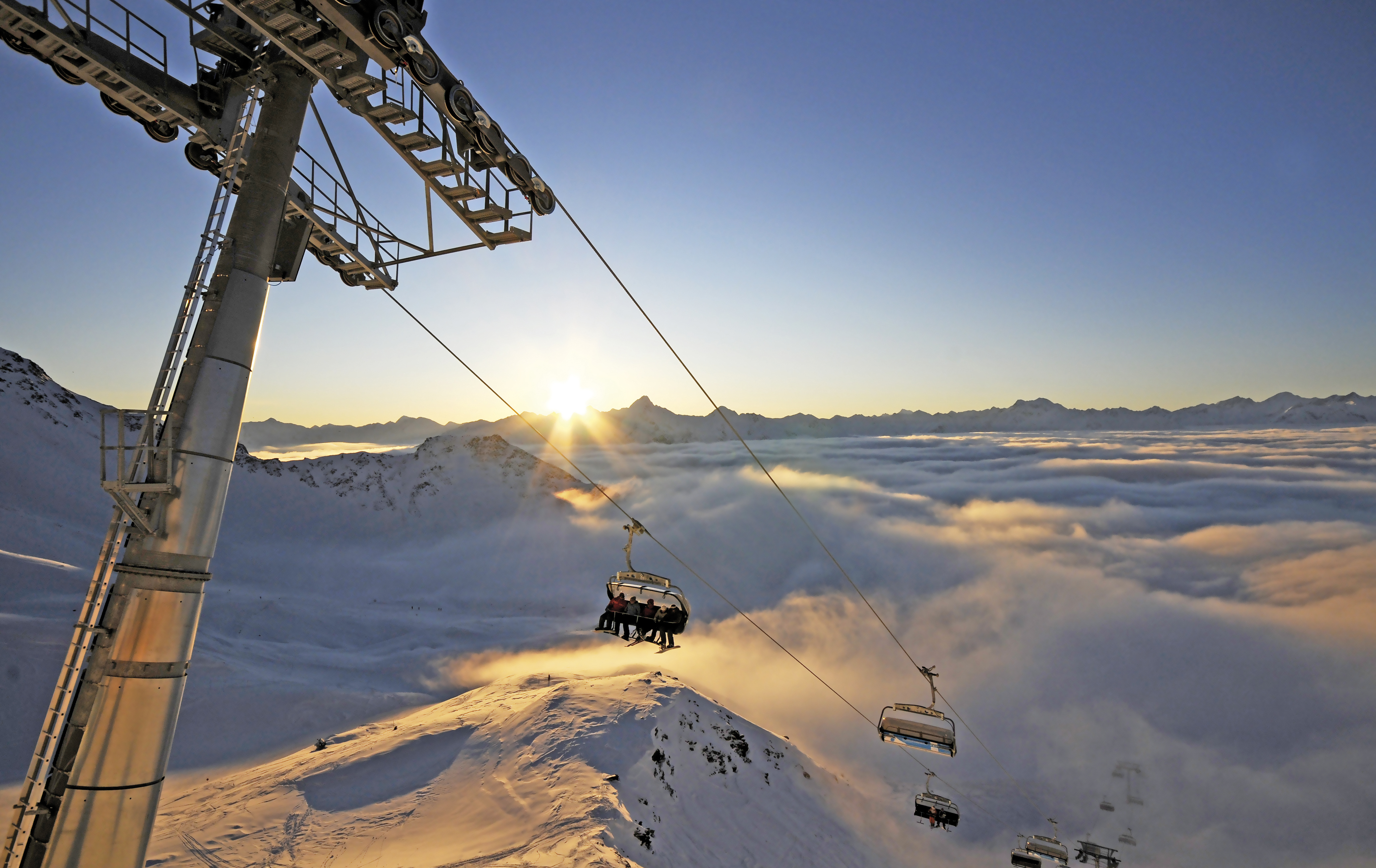 Die Sesselbahn im Großglockner-Resort erhebt sich über den schneebedeckten Bergen mit der aufgehen Sonne dahinter.